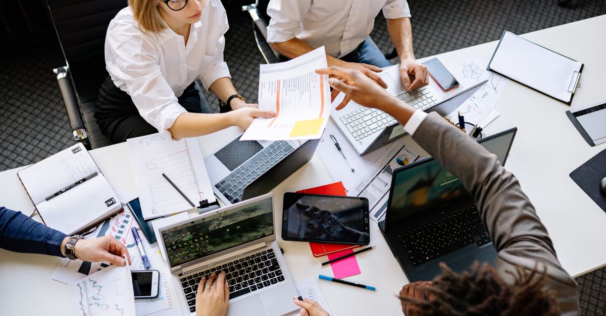 Diverse team collaborating in a modern office with laptops and documents.